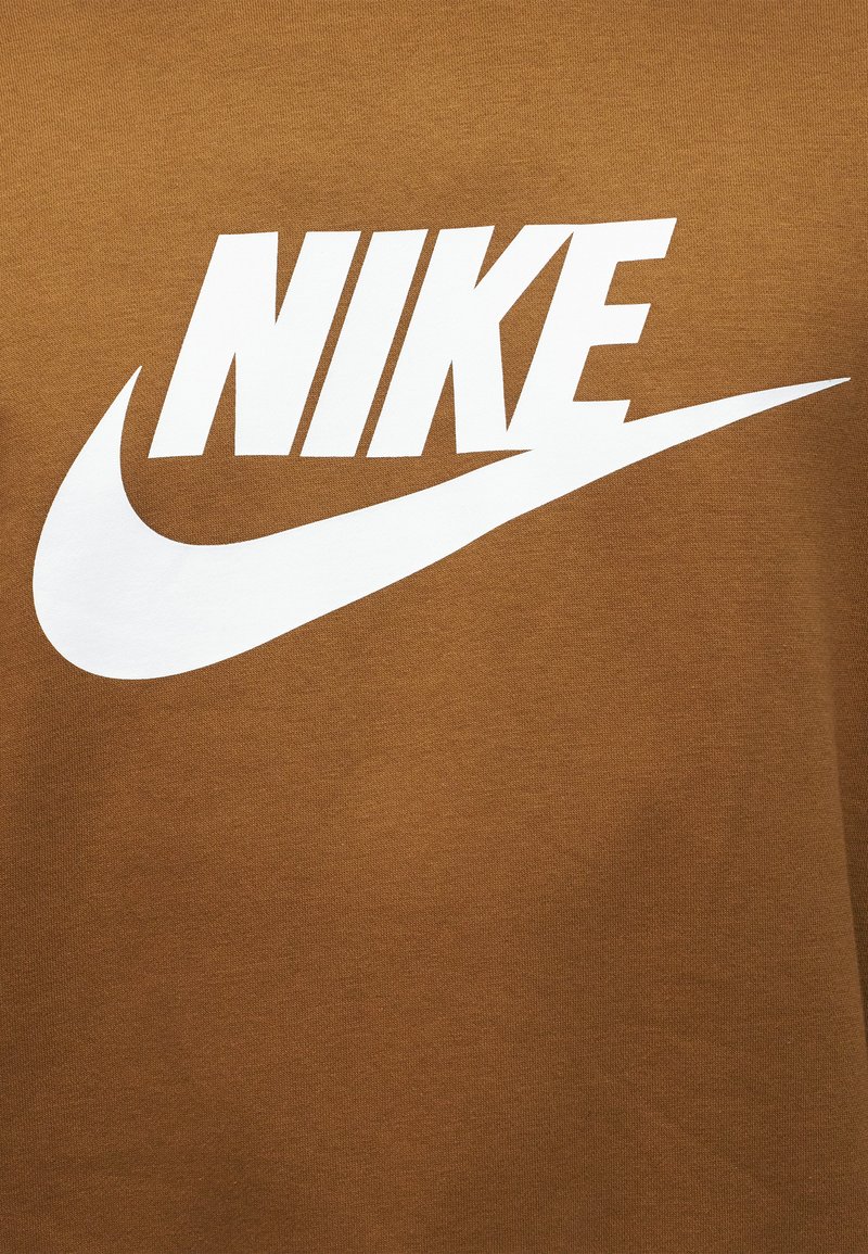 Weißes Nike-Logo mit fettem Text und Swoosh auf braunem Stoffhintergrund.