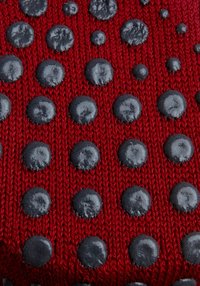 Tejido de punto rojo con patrones circulares en relieve de color negro, dispuestos de manera uniforme por toda la superficie, creando un efecto visual texturizado.
