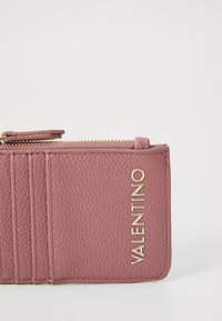 Cartera de cuero texturizado rosa con cremallera dorada, que cuenta con múltiples ranuras para tarjetas y el nombre de la marca en relieve "VALENTINO" en la parte frontal.
