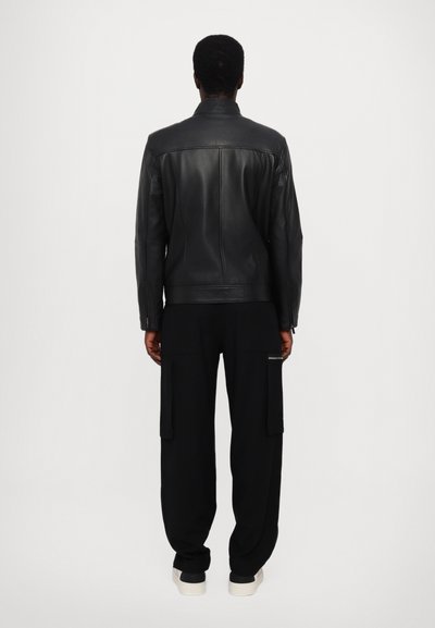Svart läderjacka med rak skärning, knäppt krage och minimalistisk design, tillsammans med lösa svarta cargobyxor och sneakers.