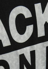 Černé tričko s velkým bílým textem. Tkanina je měkká a mírně texturovaná. Text obsahuje ostré písmo s kontrastními odstíny.