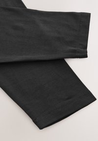 Manches longues noires de chemise qui se chevauchent sur un fond clair, montrant les détails fins des coutures aux poignets.
