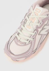 Pantof sport roz deschis și lavandă, cu partea superioară din plasă, detalii texturate și șireturi. Logo notabil pe lateral și talpă amortizată.