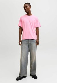 Camiseta de algodón rosa con mangas cortas y texto blanco en el frente, combinada con jeans de pierna ancha de color gris claro y zapatos negros de estilo grueso.