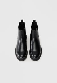 Botas de tobillo de cuero negro con un acabado suave, paneles laterales elásticos y lengüetas de tirón; forma de punta redonda y suelas de goma gruesas.