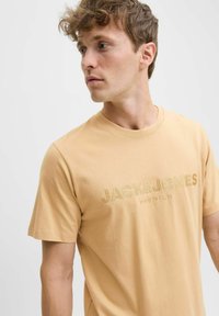Majica kratkih rukava, okruglog izreza, u svijetlo bež pamuku, s utisnutim tekstom "JACK & JONES PREMIUM" na prsima.
