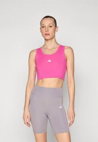 Rožinės spalvos trumpinta palaidinė su apvalia iškirpte, derinama su šviesiai pilkomis aukšto liemens dviračių šortais, ant kurių abiejų yra subtilūs logotipo akcentai.