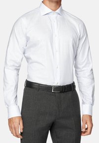 Vit skjorta med ljusblå ränder, knappad krage, långa ärmar, i kombination med mörkgrå byxor och ett svart läderbälte.