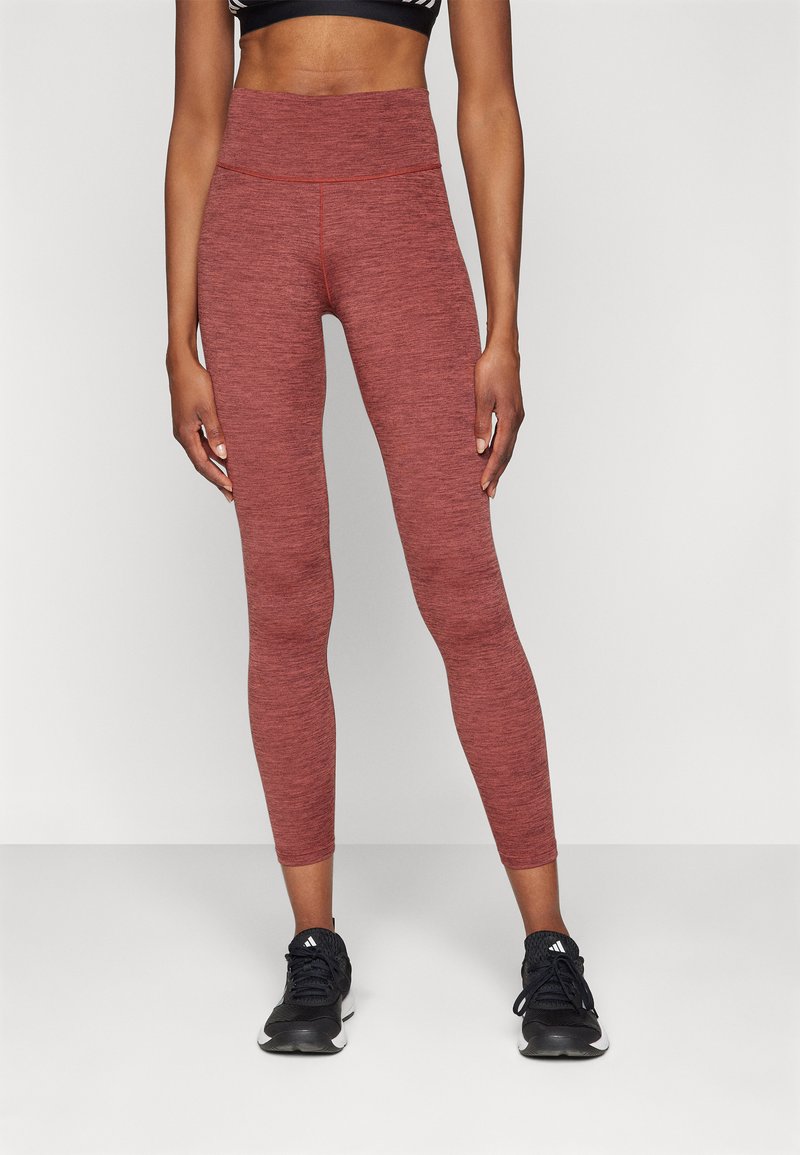 Leggings de sport taille haute, maron, en tissu extensible avec une texture chinée, associés à des baskets noires.