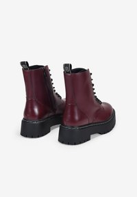 Botines de cuero burdeos con cordones, cremallera lateral, lengüetas negras, suelas de plataforma negras gruesas y detalles de costura blanca.
