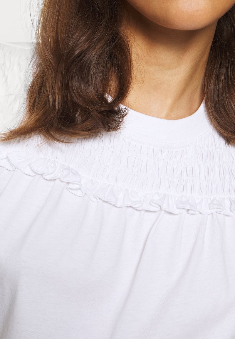 Vit t-shirt med en texturerad samlad halslinning med volanger, korta ärmar och en mjuk tygfinish.