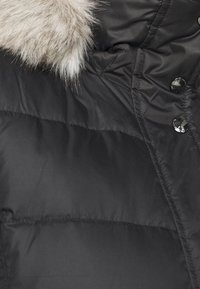 Chaqueta puffer negra con un suave y ligero borde de piel sintética gris claro en la capucha, botones a presión negros brillantes y textura acolchada.