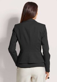 Schwarze maßgeschneiderte Blazerjacke mit einem Taillengürtel, strukturierten Schulternähten und langen Ärmeln. Glattes Material mit matter Oberfläche.