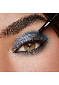 Primer plano de un ojo con sombra de ojos azul y plata, delineador negro aplicado y pestañas oscuras. El iris es marrón con una textura brillante.