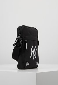 Borsa a tracolla nera con chiusura a zip, caratterizzata da un grande logo bianco dei New York Yankees, tracolla regolabile e texture in tessuto.
