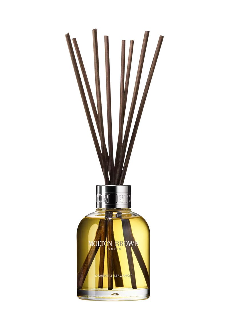 Reed diffuser with clear glass bottle, silver collar, yellow liquid, and eight brown reeds. Label reads "Molton Brown, Orange & Bergamot."