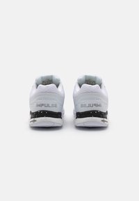 Scarpe sportive bianche con una parte superiore testurizzata, suola nera con un motivo maculato e il marchio "IMPULSE" sul tallone.
