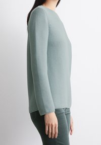 Světlá zelená pletená svetr s kulatým výstřihem a dlouhými rukávy. Texturovaný vzor a rovný lem. Spárováno s tmavě zelenými kalhotami.