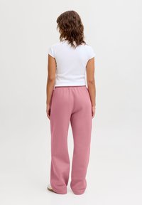 Bílý top s krátkými rukávy ve spojení s volnými růžovými tepláky s elastickým pasem, hladkou texturou a rovnými nohavicemi.