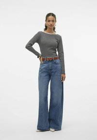 Zwart-wit gestreepte lange mouwen top, gecombineerd met brede blauwe denim jeans, een bruine riem en crèmekleurige hakken. Eenvoudig ontwerp en casual pasvorm.