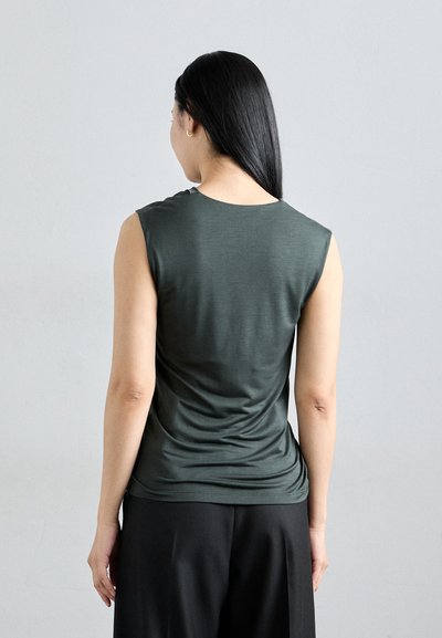 Sleeveless, dark green top made from smooth fabric, featuring a round neckline and gathered detail at the back, paired with black trousers.