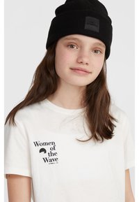 Vit t-shirt med korta ärmar och svart text "Women of the Wave" samt en svart grafik. Bärs med en svart ribbad beanie med en logotyp-patch.