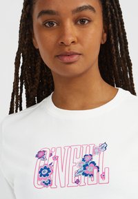 Vit kortärmad t-shirt med färgglad blommig broderi i blått och rosa, med varumärket "O'NEILL" i fet rosa text.