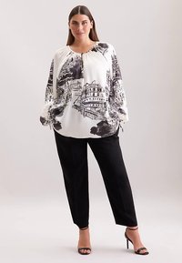 Weiße Bluse mit einem schwarzen Stadtbild-Print, rundem Ausschnitt und Ballonärmeln, kombiniert mit schwarzer Hose und Riemchenabsätzen.