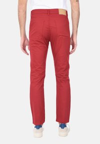 Pantaloni aderenti rossi in cotone con una texture liscia, dotati di due tasche posteriori e un'etichetta in pelle marrone in vita.