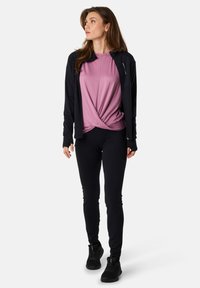 Musta zip-up takki vaaleanpunaisen solmitun topin päällä, yhdistettynä mustiin tiukkoihin legginsseihin ja mustiin urheilukenkiin. Sujuva kangas ja tyylikäs muotoilu.