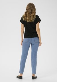 Black short-sleeve top with diamond pattern, paired with light blue slim-fit jeans and black slip-on flats; model shown from behind.