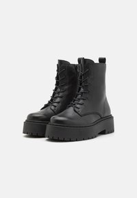 Botas de cuero negra hasta el tobillo con frente con cordones, cremallera lateral y suela de goma gruesa. Presentan una textura suave y un diseño robusto.