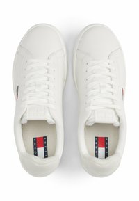 Weiße synthetische Sneaker mit glatter Textur, flachen Schnürsenkeln, runder Zehenpartie und einem kleinen Logoetikett in Rot, Weiß und Blau auf der Zunge.