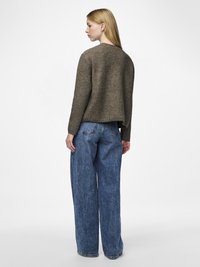 Brun stickad tröja med lös passform och ribbad textur, kombinerad med höga ljusblå vida jeans. Enkel bakvy.