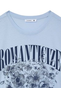 T-shirt azzurro chiaro con una stampa grafica di fiori e la parola "ROMANTICIZE" in lettere nere in grassetto. Tessuto di cotone liscio, scollo a girocollo.