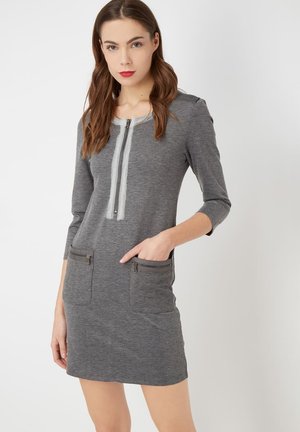 Vestido gris de tejido de punto, con cierre frontal de cremallera y dos bolsillos con cremallera. Mangas tres cuartos y un silueta ajustada.