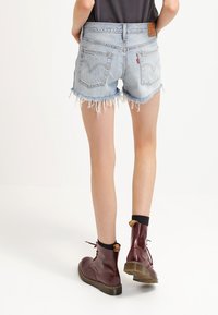 Ljust blå denimshorts med fransad nederkant, bakfickor och en läderlapp. Kombineras med burgundy snörstövlar och svarta strumpor.