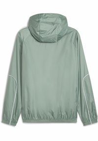 Lys grønn vindjakke med hette, elastiske mansjetter og kant, med hvit dekorativ piping langs ermene. Glatt, vannavvisende overflate.