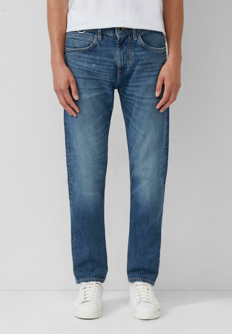 Jeans en denim bleu avec une coupe droite, finition délavée, cinq poches, fermeture à bouton et baskets blanches. Texture de tissu légère.
