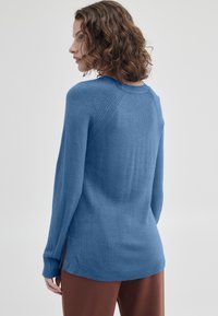 Ljusblå stickad tröja med rundad halsringning, ribbade ärmslut och sidofickor; mjuk textur, avslappnad passform och subtil sömdetaljering på axlarna.