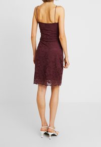 Weinrote Spitzenkleid mit dünnen Trägern, tailliertem Oberteil und gewelltem Saum. Kombiniert mit weißen Riemchen-Heels, die eine florale Textur zeigen.