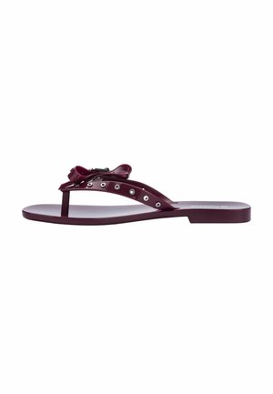 Flache lila Flip-Flop-Sandale mit Zehensteg, verziert mit metallischen Ösen und einer Schleife am Riemen.
