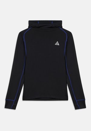 Chemise à manches longues noire avec capuche, coutures bleues et petit logo triangle blanc ACG sur la poitrine gauche, sur fond blanc.