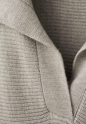 Vêtement en maille grise texturée avec un large col, présentant un motif côtelé et un matériau doux et chaud. Lignes épurées et détails subtils.