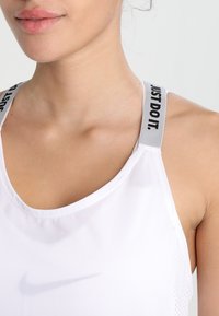 Witte sporttanktop zonder mouwen met een ronde hals, voorzien van zwart en grijs "JUST DO IT"-tekst op de schouderbanden en een subtiele Nike-logo.