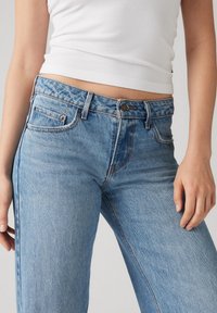 Light blue denim jeans with a high waist, five pockets, and a button closure. The fabric has a textured, slightly faded appearance.