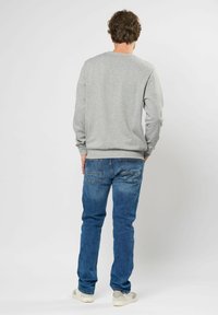 Grijze sweatshirt met lange mouwen, ronde halslijn en geribbelde manchetten, gedragen met blauwe spijkerbroeken en lichtgekleurde sneakers.