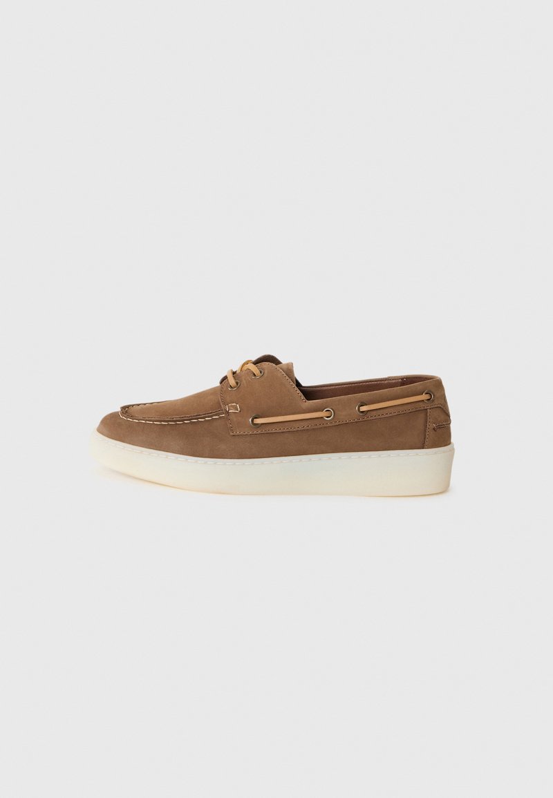 Bateau en daim marron avec une semelle en caoutchouc crème, un détail de lacet et un contraste de couture, présentant un design à profil bas et une construction légère.