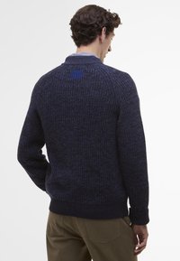 Marineblauwe gebreide trui met een textuurpatroon, voorzien van een opstaande kraag en een blauwe accent aan de achterkant. Geribde manchetten en tailleband.