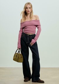 Žebrovaný růžový crop top s odhalenými rameny, tmavé denimové kalhoty s vysokým pasem a rozšířenými nohavicemi, zelená prošívaná kabelka s hnědými držadly a hnědé mokasíny.